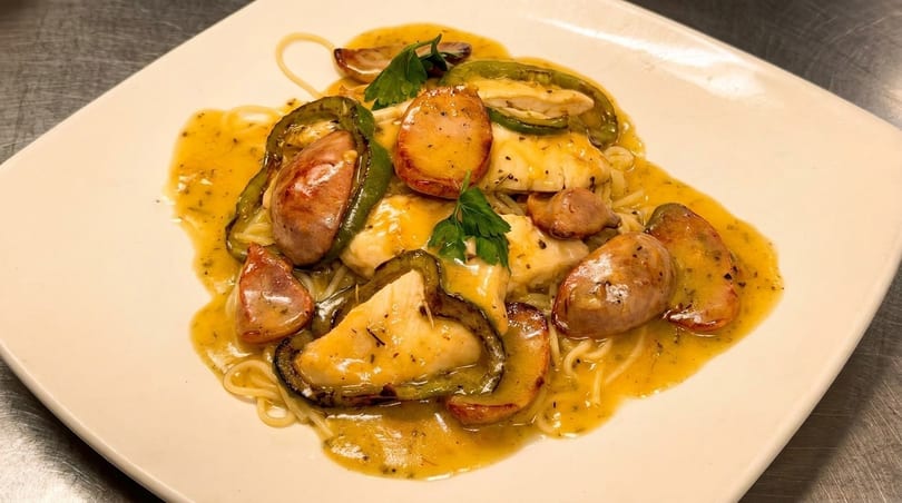 Spaghetti with chicken, sausage, green peppers, and a creamy yellow sauce on a white plate.