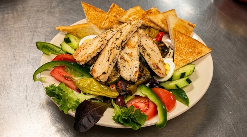 Grilled chicken salad with mixed greens, tomatoes, cucumbers, peppers, hard-boiled eggs, and toast.
